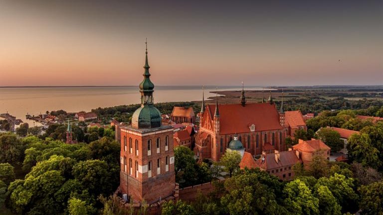 Great view of the beautiful city of Frombork located in Warmia, Poland. Cathedral Hill among trees at sunset shutterstock_2209500045.jpg